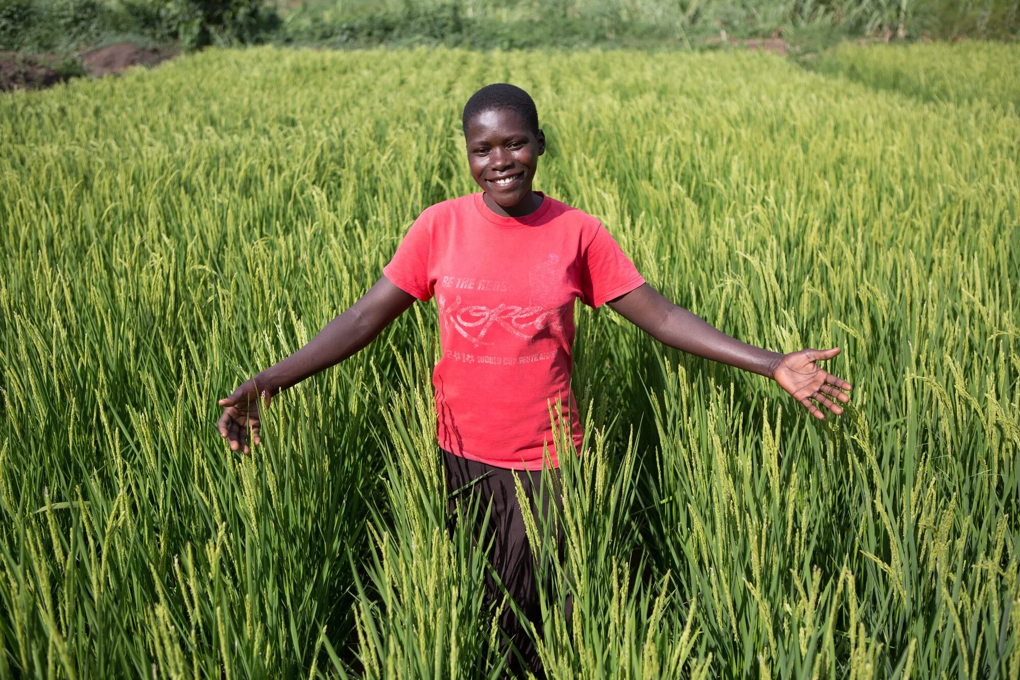 A woman standing in a green rice field with her arms open