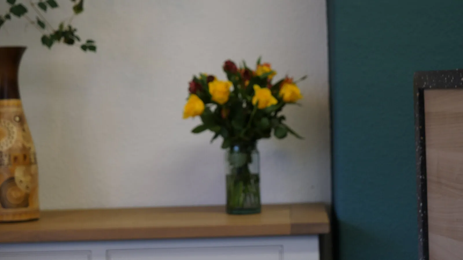 The empty interview set before the first take: a sideboard, a vase of yellow flowers and the practice’s teal wall
