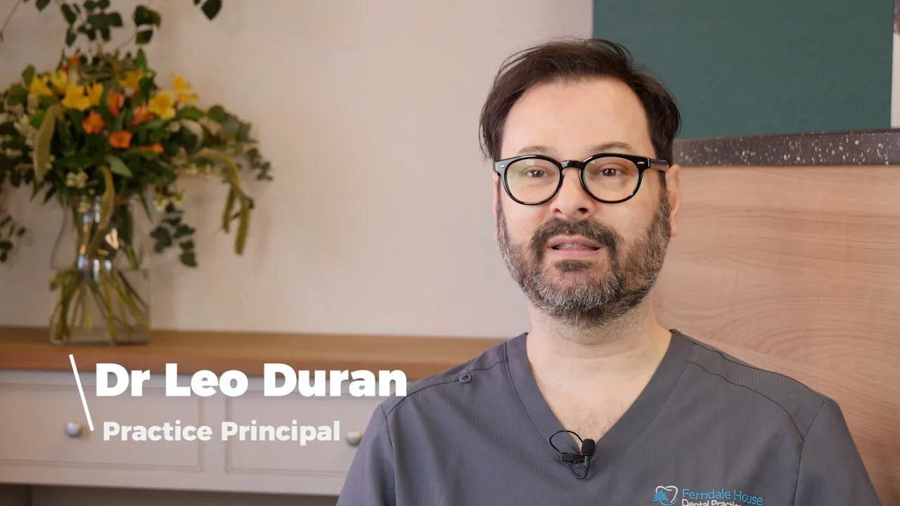Dr Leo Duran, Practice Principal, introducing the practice in front of the teal wall and a vase of yellow flowers