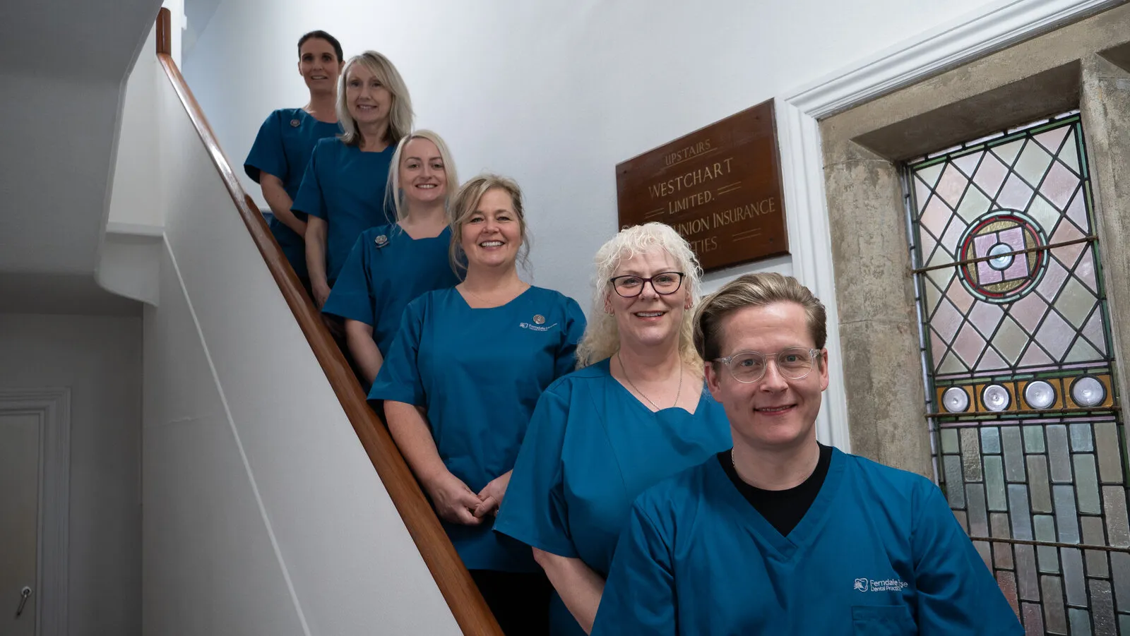 The nurses and reception team on the stairs beside the stained-glass window