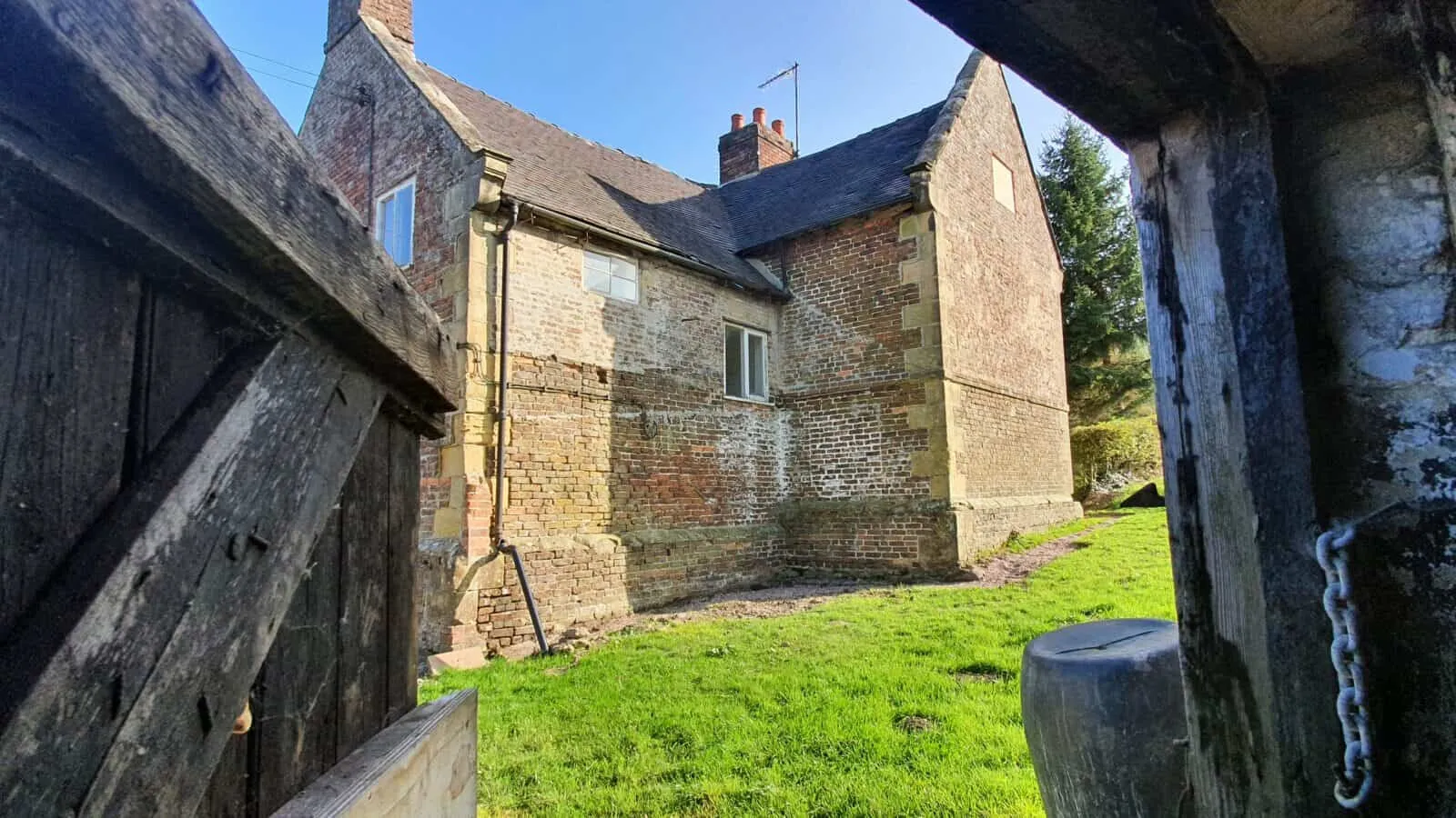 A stone farmhouse seen through an old timber barn door, from OakenStone’s website