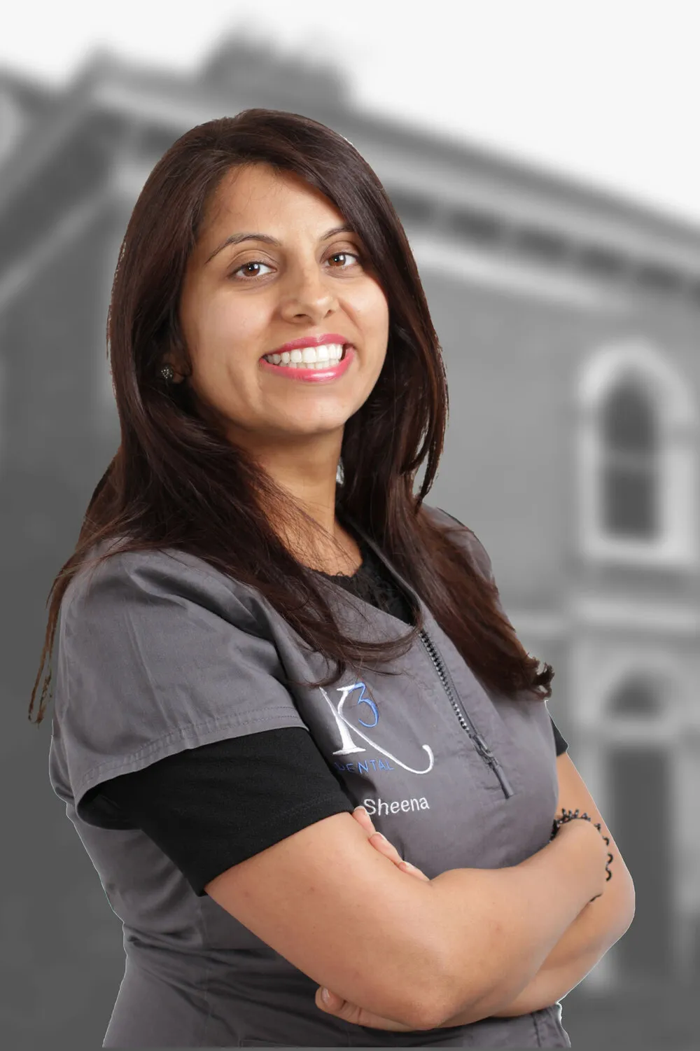 Dr Sheena Kotecha, arms folded, in K3 scrubs in front of the building in black and white