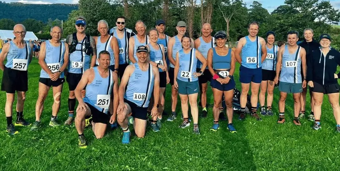 About twenty Matlock runners in their pale blue club vests and race numbers, lined up on the grass before a race