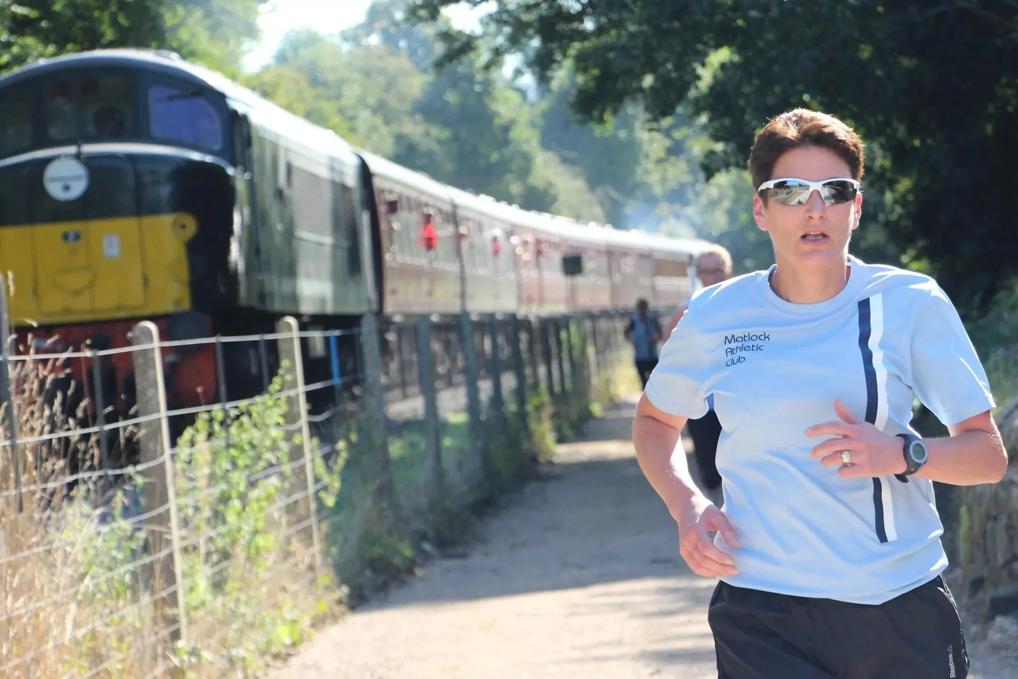 A runner in a Matlock Athletic Club T-shirt on a trail beside a heritage diesel train