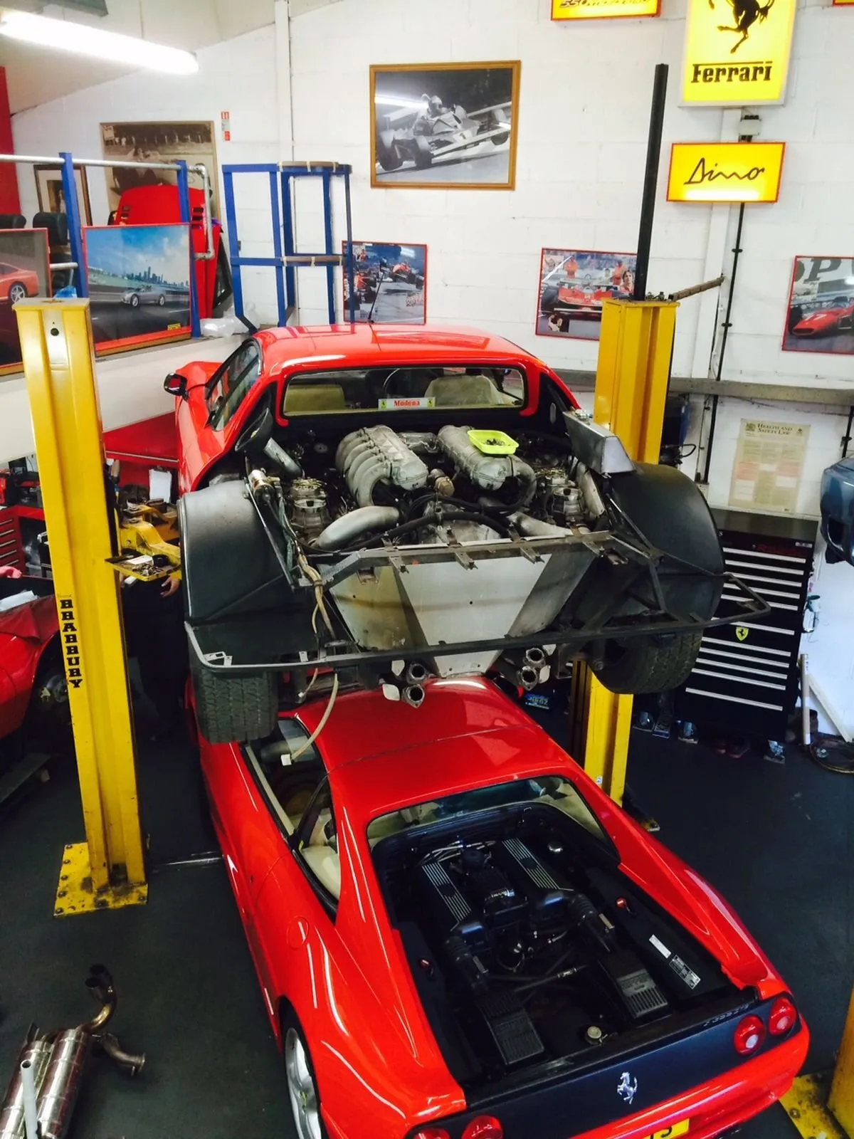 A Ferrari 355 on a lift in the workshop, its engine lowered out, under Ferrari and Dino signs