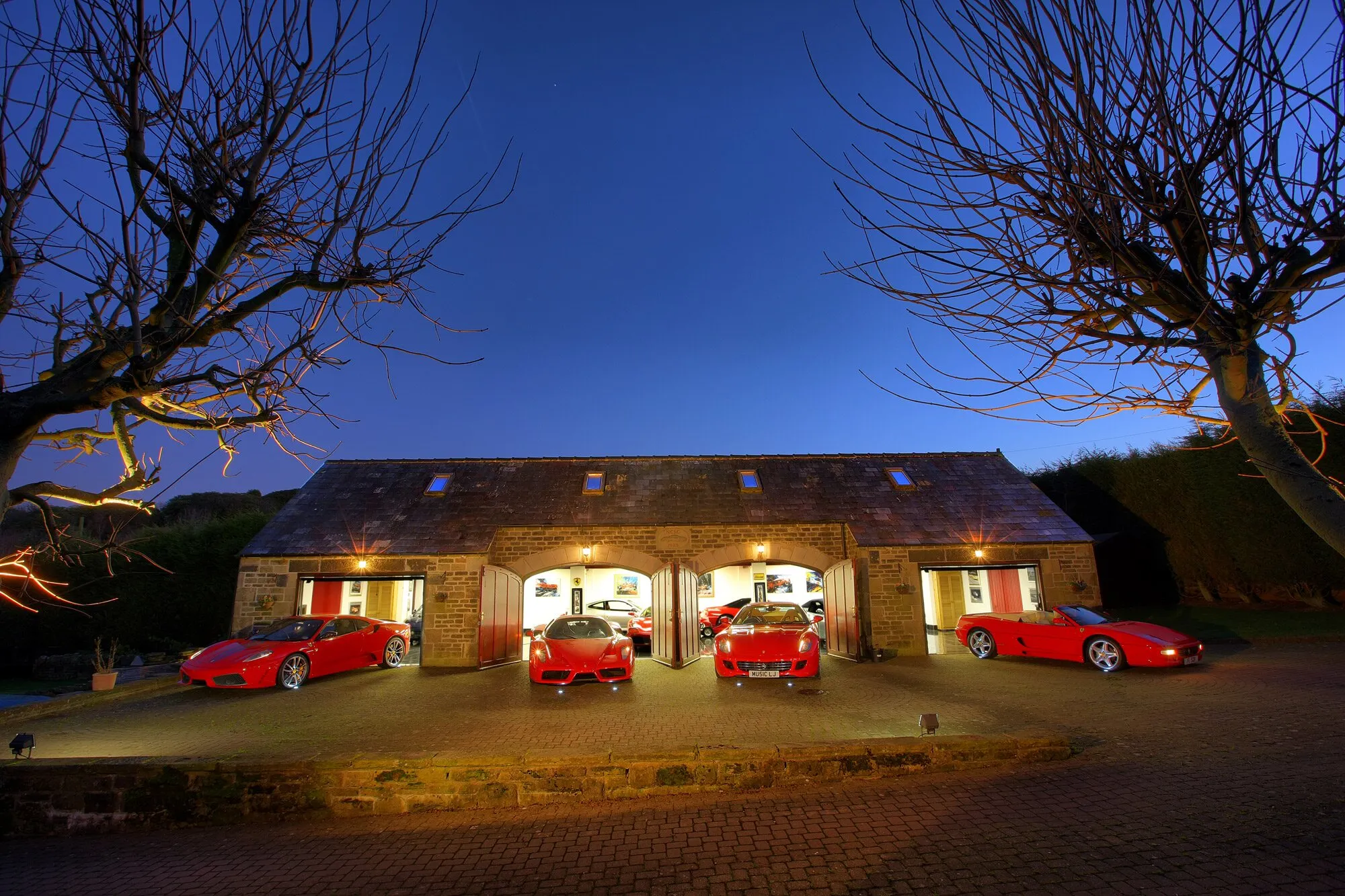 The stone barn showroom at dusk, with four red Ferraris on the forecourt
