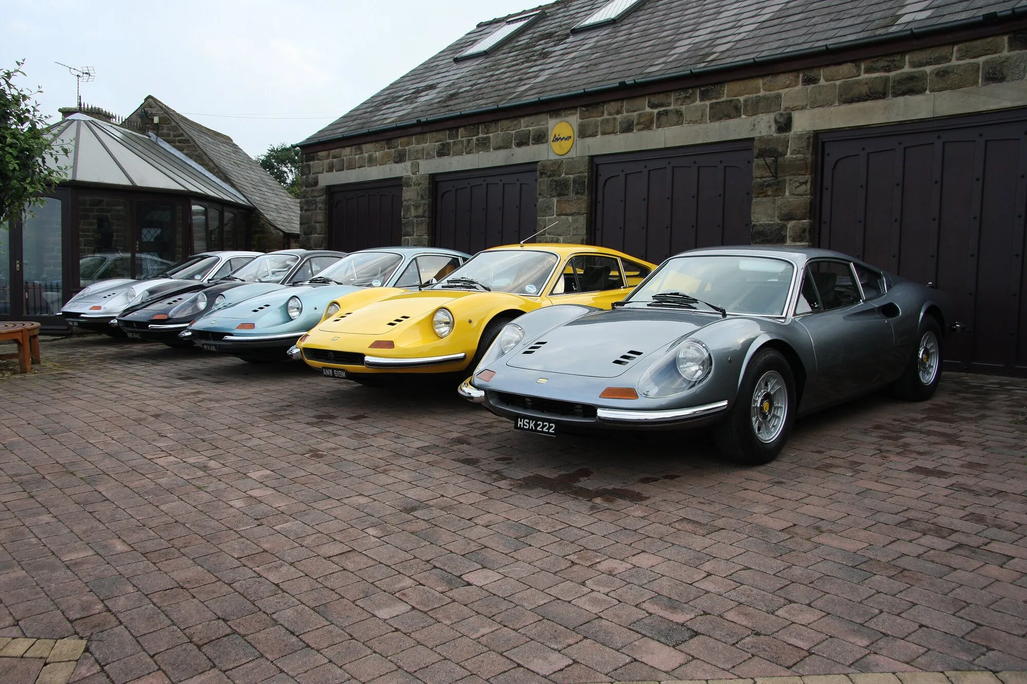 Seven Ferrari Dinos lined up in front of the stone garages