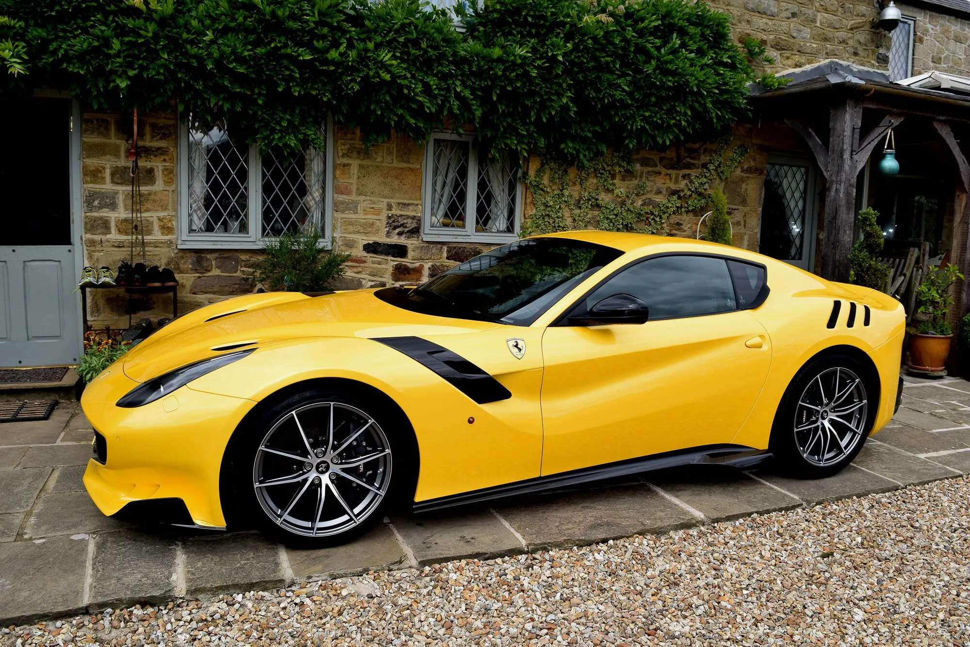 A yellow Ferrari F12tdf parked beside a stone cottage