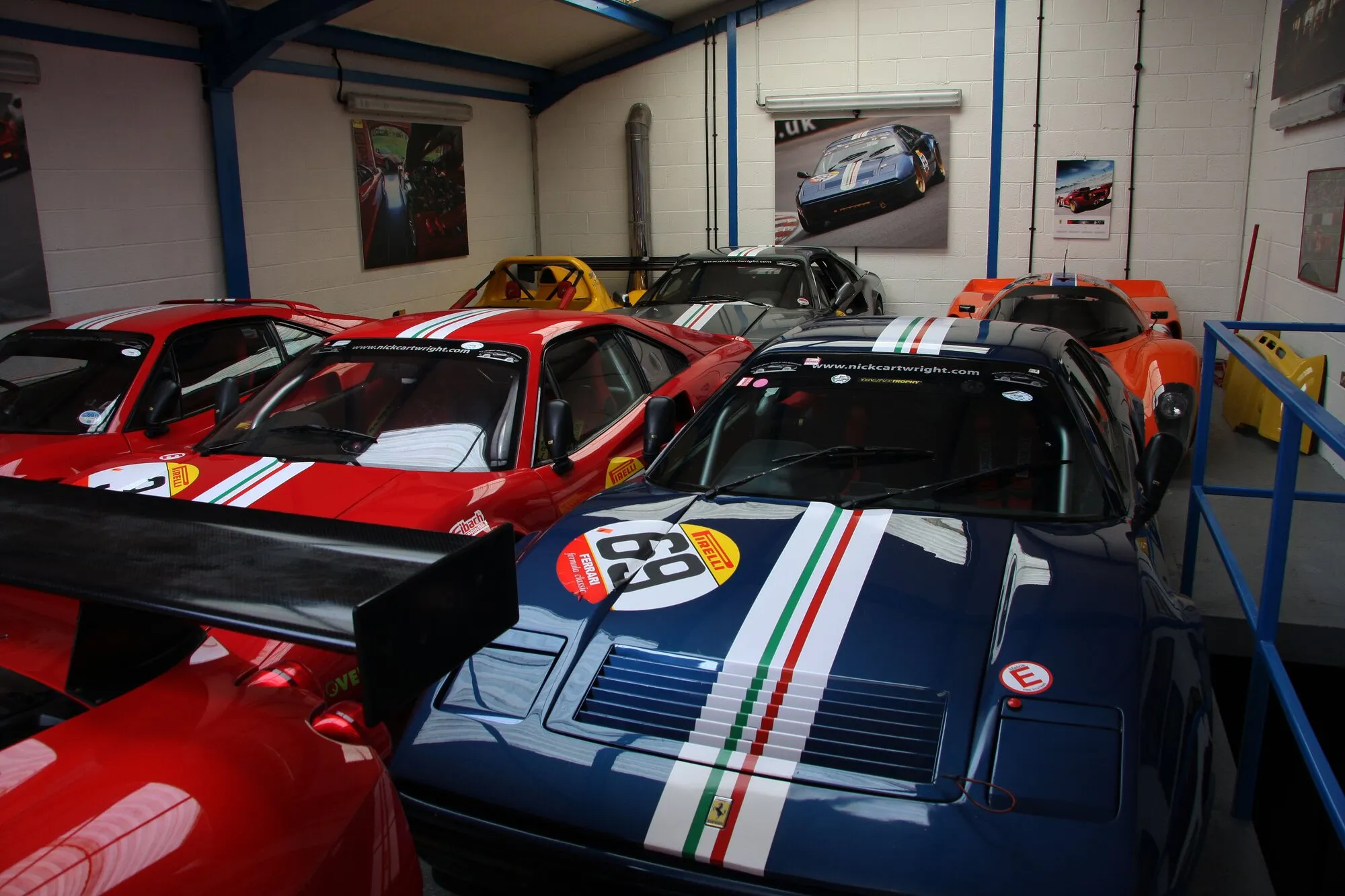 The racing stable: Ferraris in racing livery side by side in the workshop, one blue with a green, white and red stripe