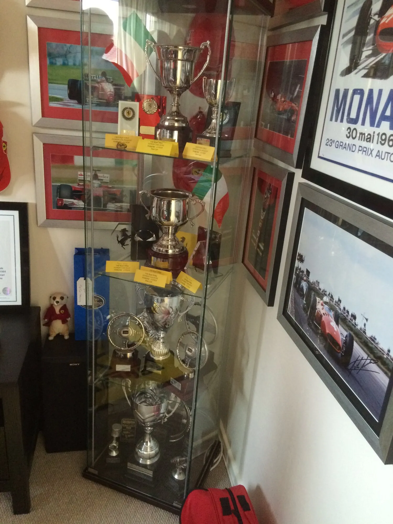 A cabinet of racing trophies beside framed racing photographs and a Monaco Grand Prix poster
