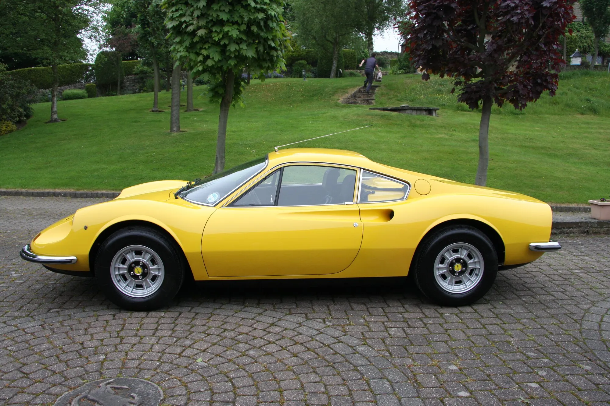 A yellow Ferrari Dino 246 GT in profile on cobbles