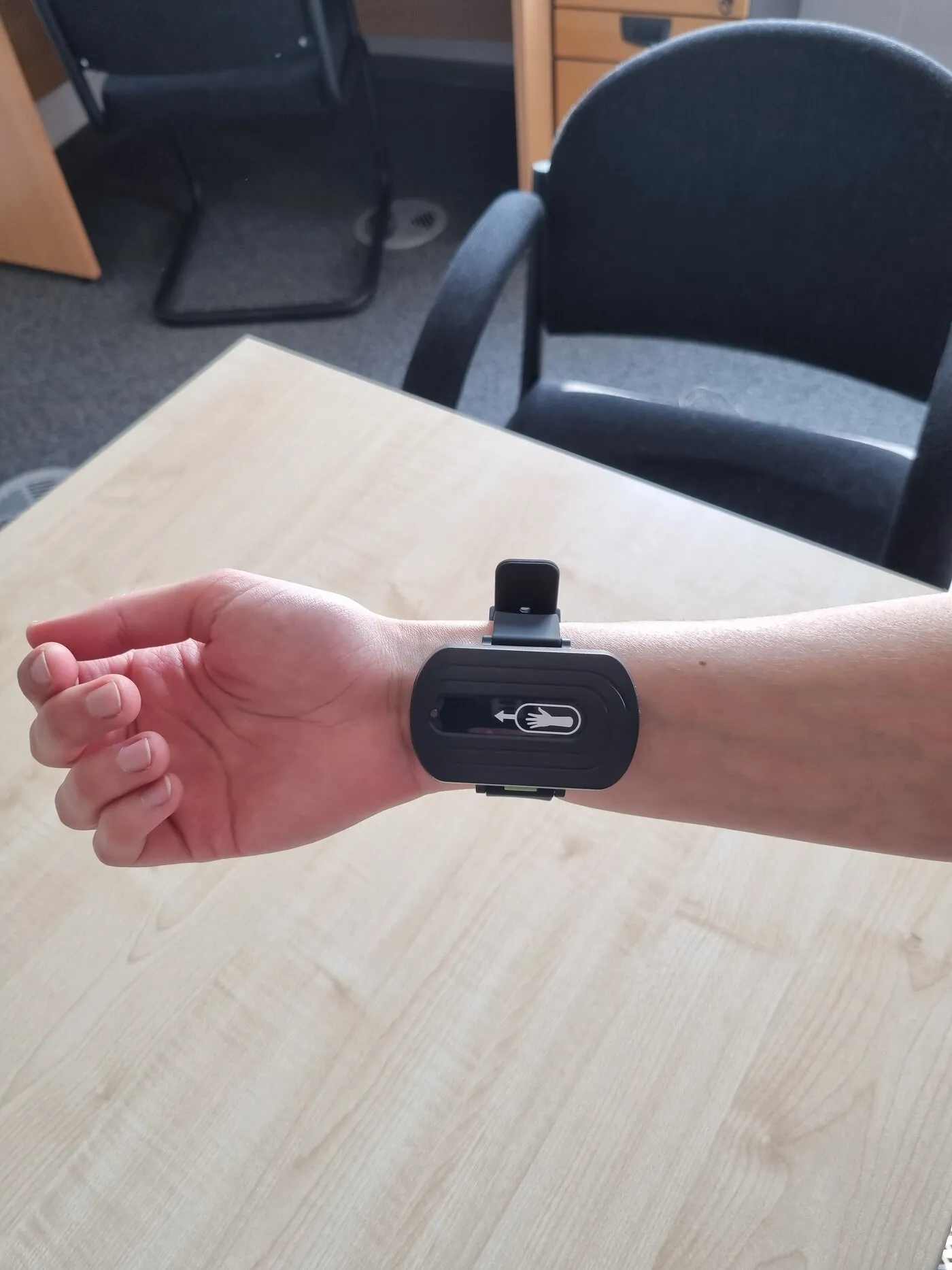 The trial prototype on a wrist resting on a desk, with office chairs behind