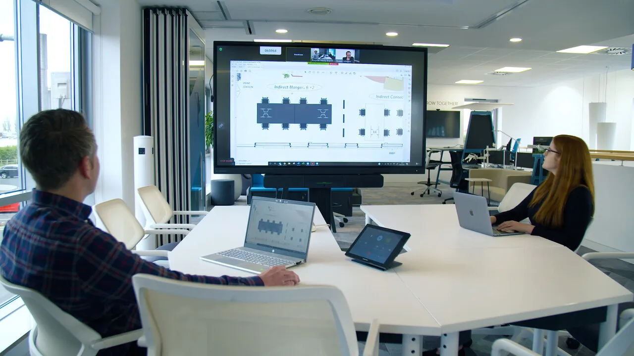 A meeting in a room with a large screen showing a floor plan