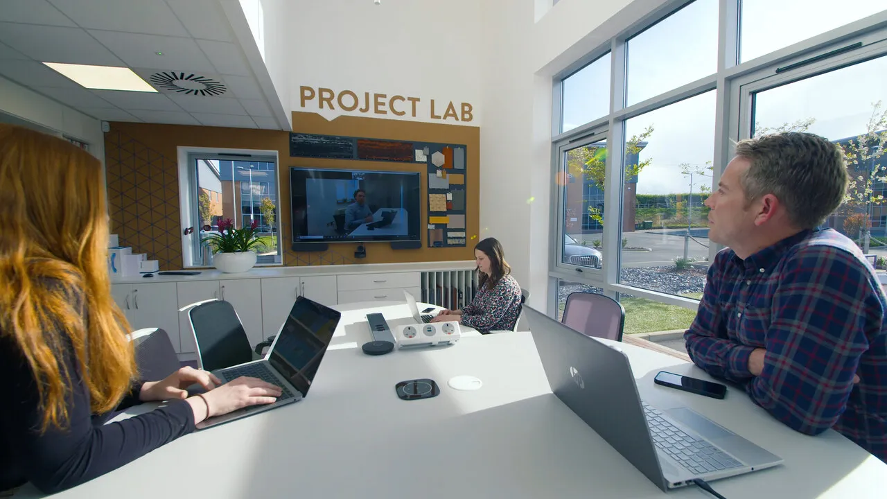 A meeting at a round table in front of the Project Lab screen