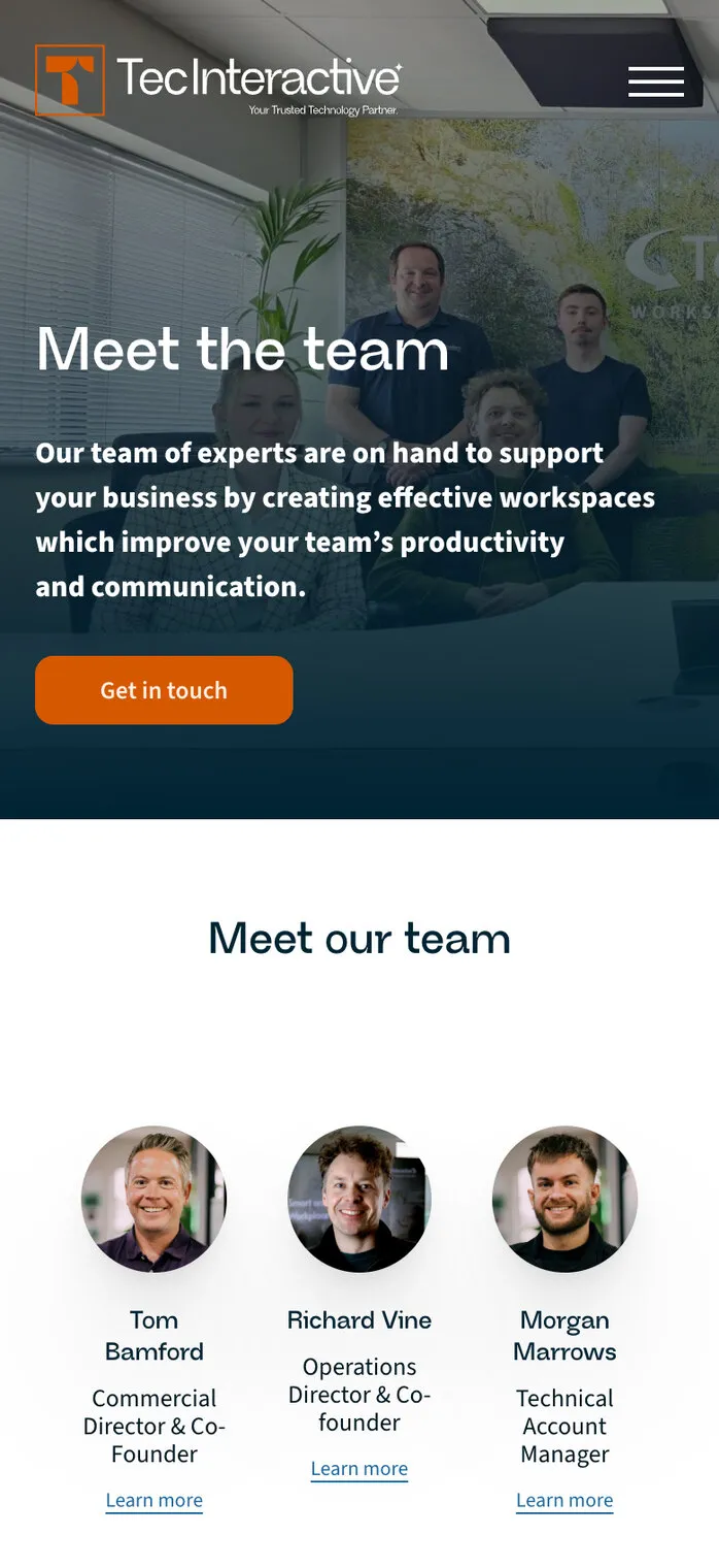 Meet the team on a phone: the team in front of the old arrows logo on the office wall