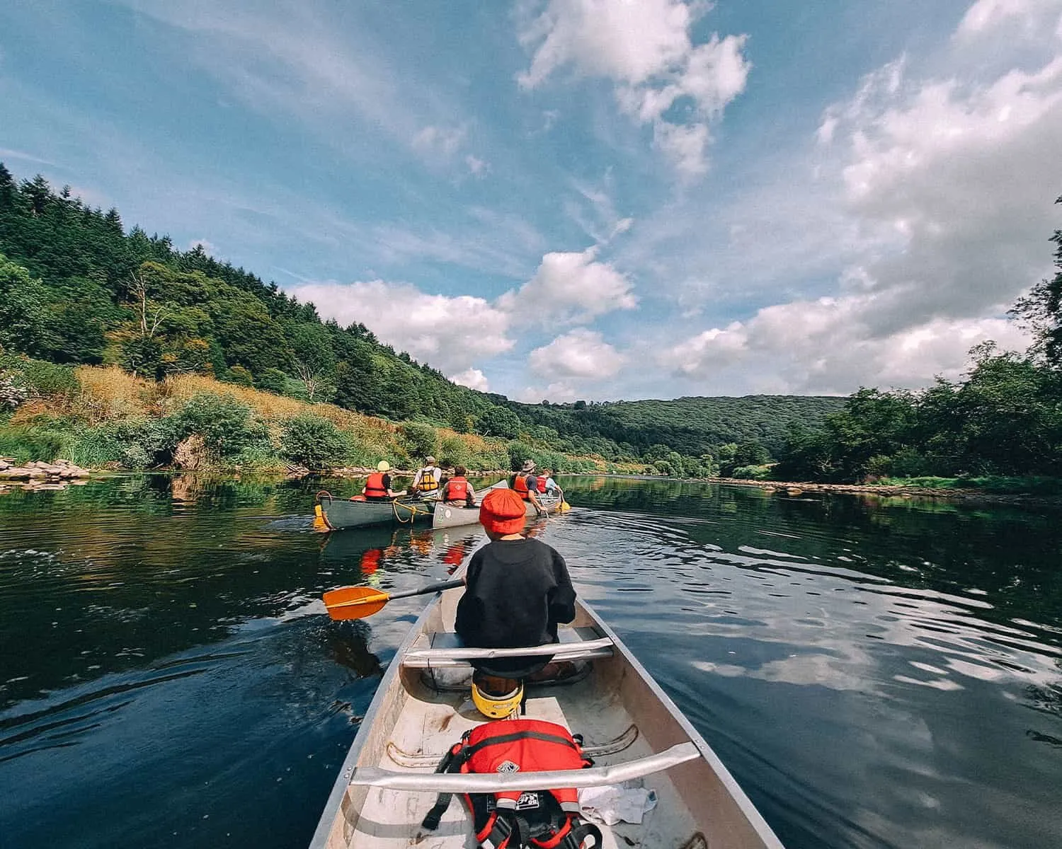 Canoeing down a river through a wooded valley, seen from the back of a canoe