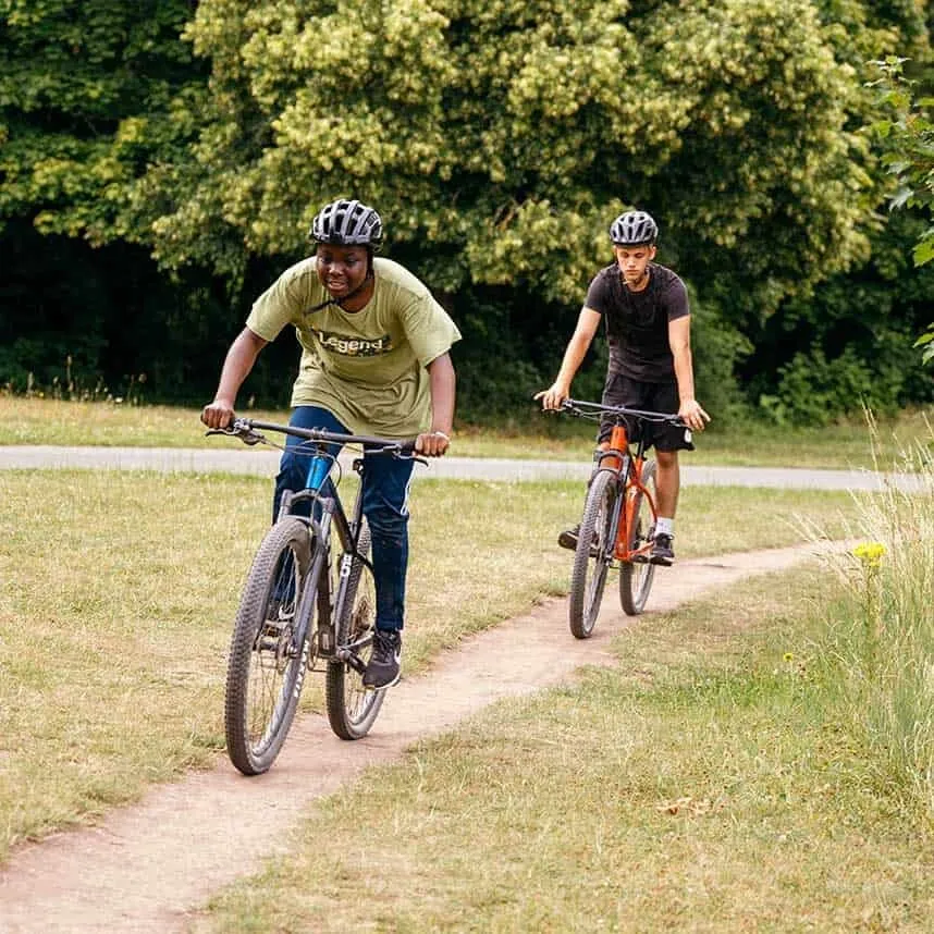Two riders on mountain bikes on a path through long grass