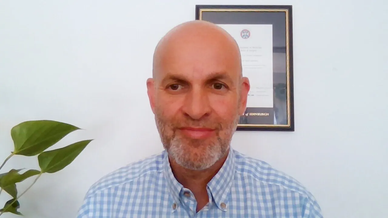 Dr Andrew Kernohan speaking to camera in his office, with the logo in the corner