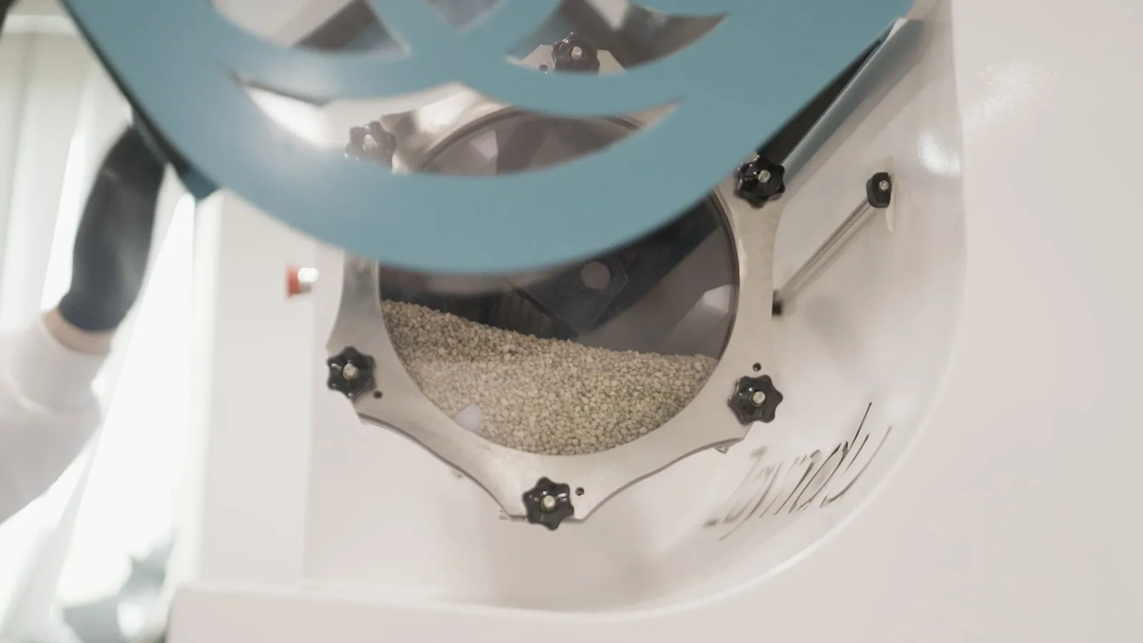 Seeds in the drum of a Zayndu machine, seen through a teal grille shaped like Zayndu’s symbol
